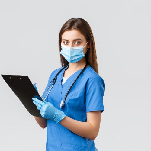 Covid-19, preventing virus, health, healthcare workers and quarantine concept. Professional female nurse or doctor in blue scrubs, medical mask and gloves, writing down patient info using clipboard.